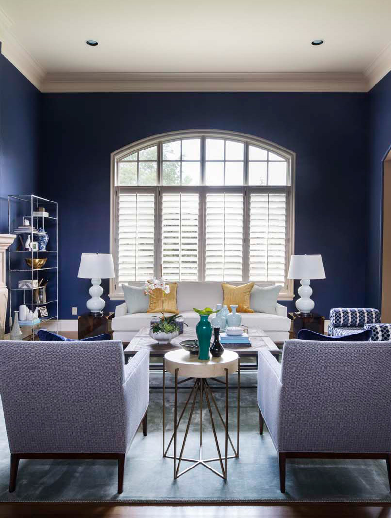 Elegant living room with navy blue walls, large arched window, and stylish furniture.