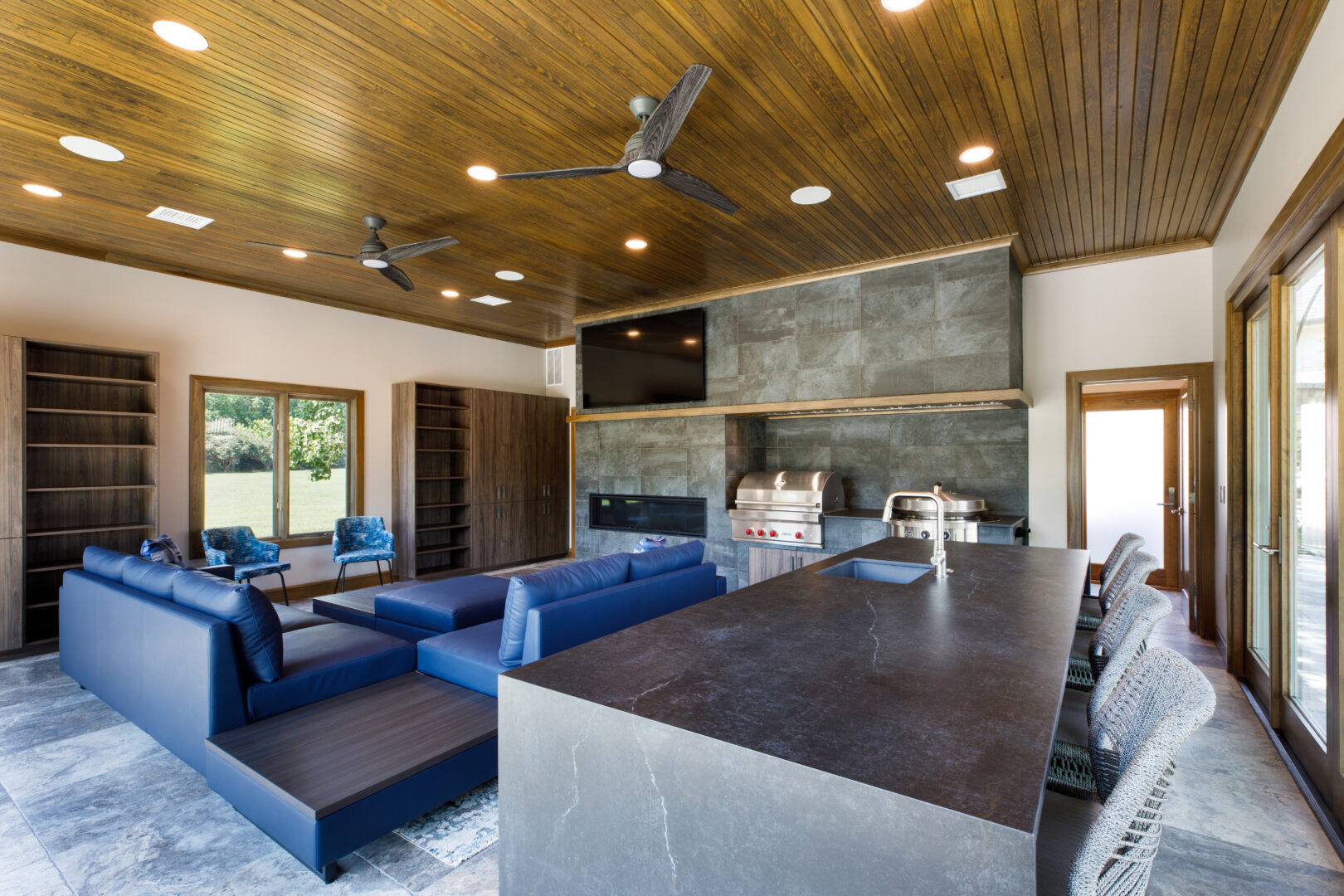 Modern living room with fireplace, blue sofas, and wooden ceiling.