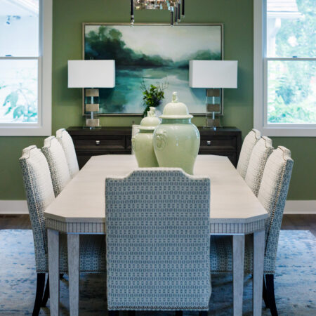 Elegant dining room with green walls, large windows, and a white table with eight chairs.