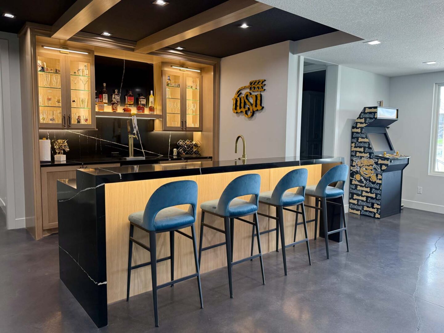 Contemporary interior featuring a sleek black and wood bar with four blue barstools and a decorative.