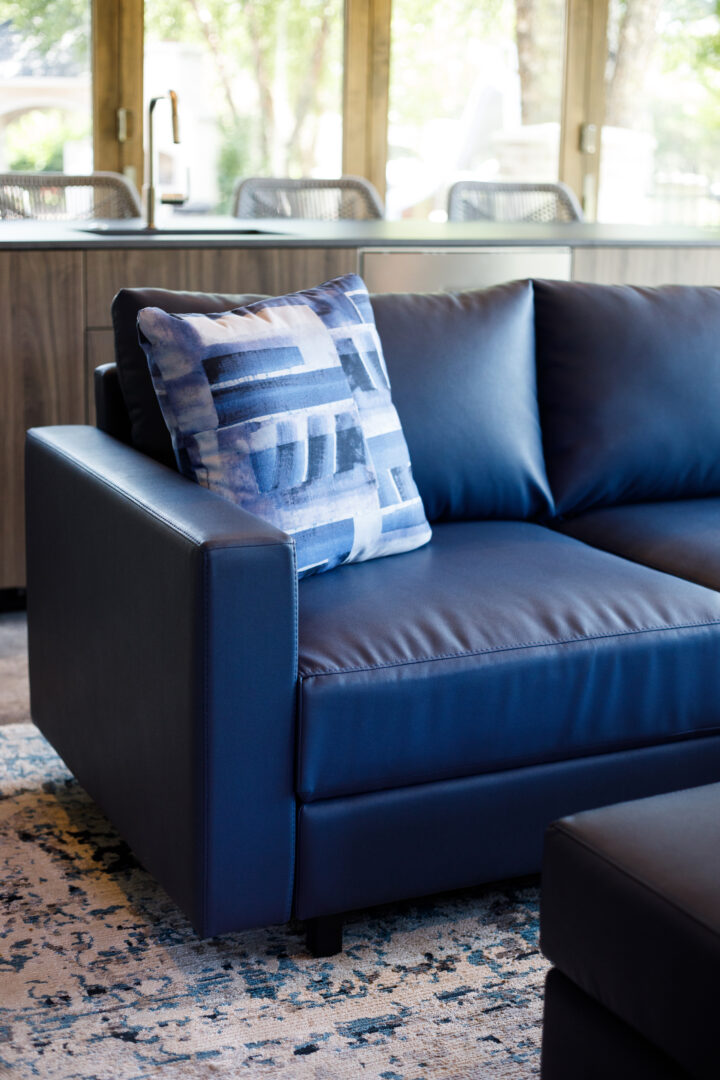 Blue leather sofa with patterned pillow in a well-lit, contemporary living space.