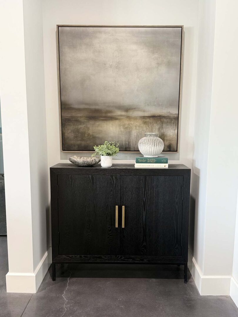 Elegant black sideboard with decorative items and abstract artwork in a contemporary interior.