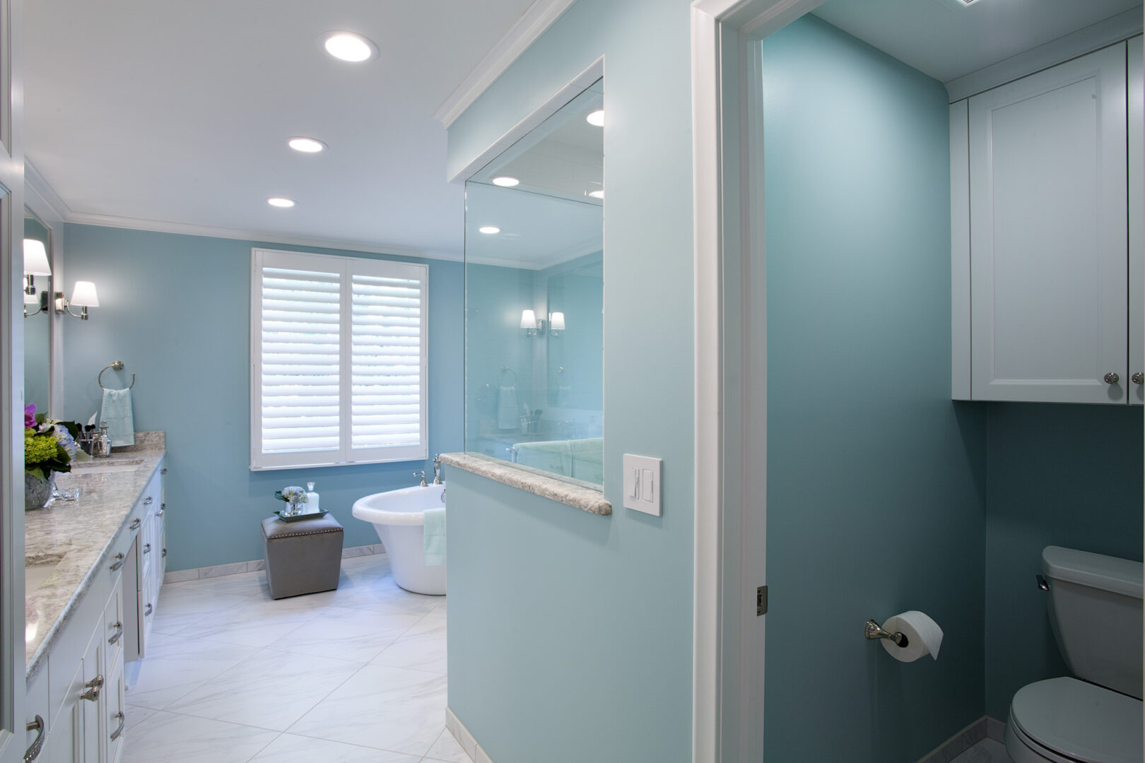 Bright blue bathroom with white cabinetry and modern fixtures, featuring a separate toilet area and.