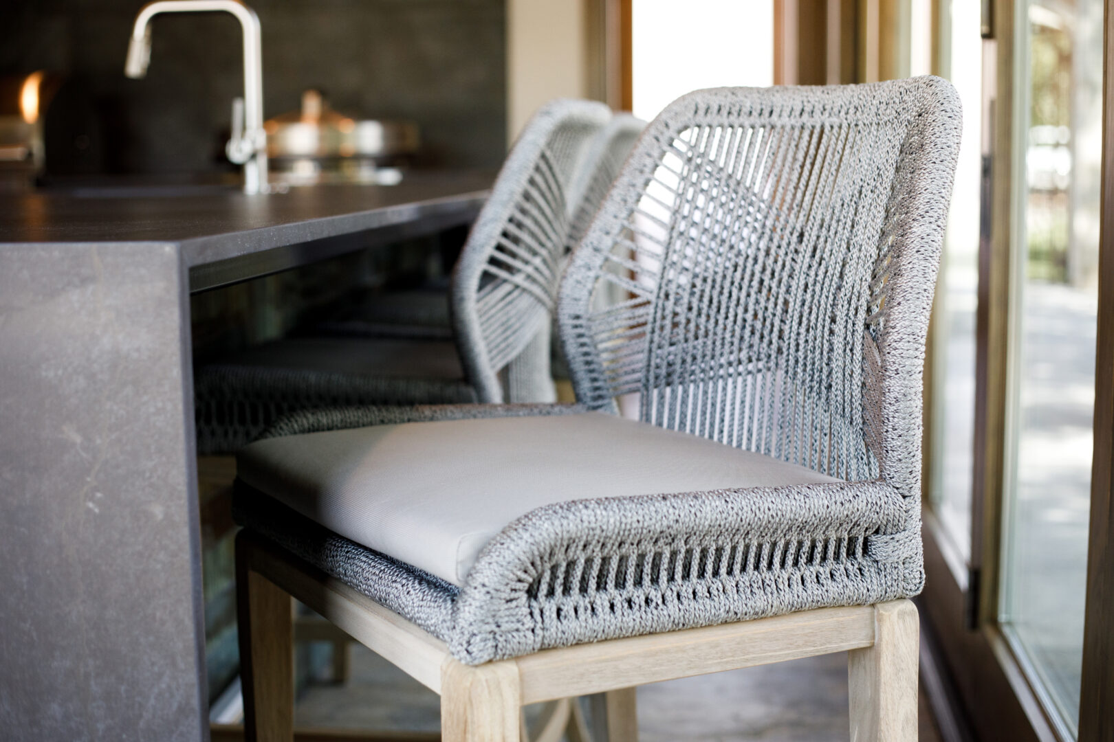 Woven dining chairs in a modern kitchen with a dark countertop and large windows.