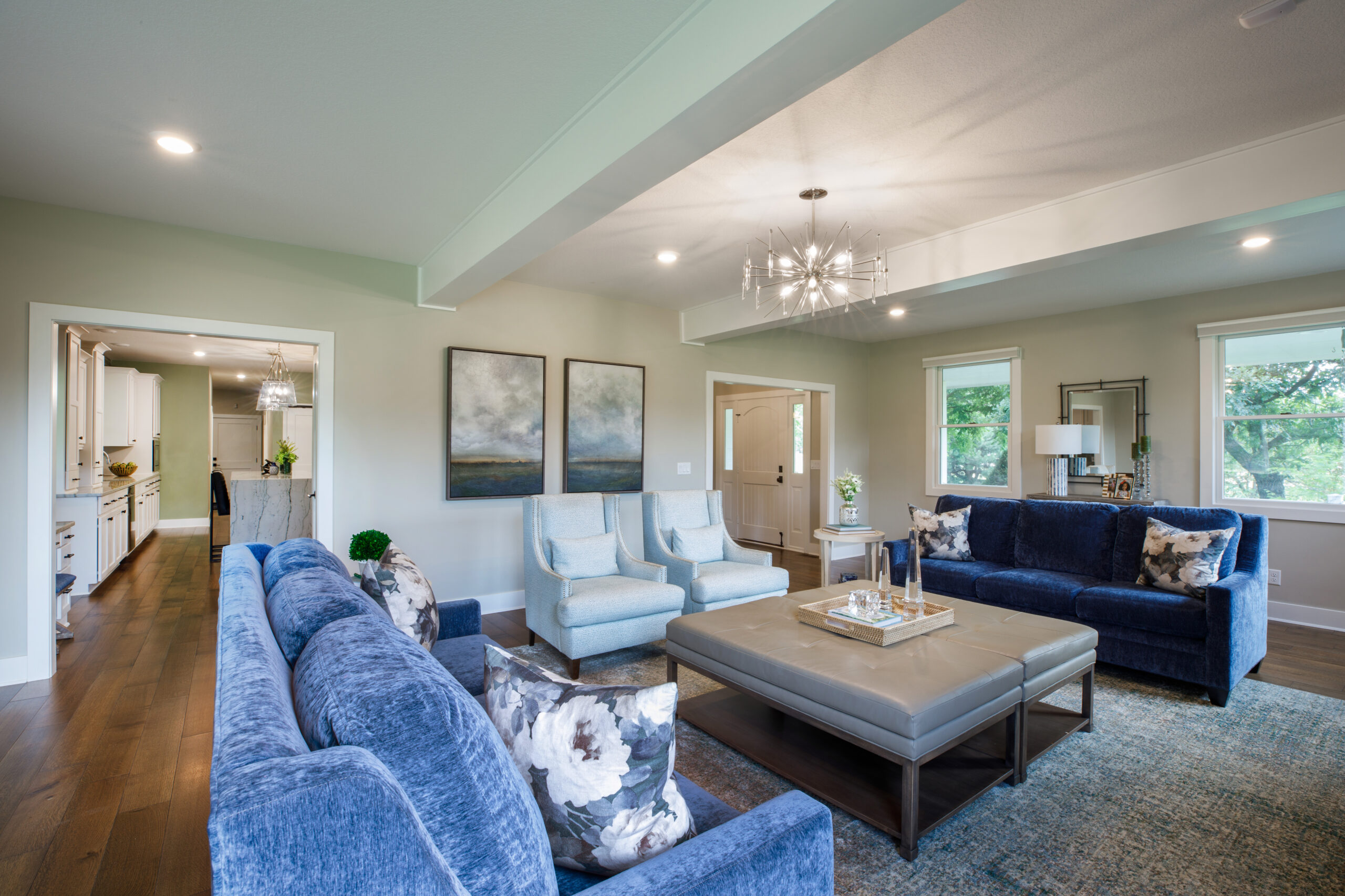 Bright and inviting living room featuring blue velvet sofas, white armchairs, and large windows that.