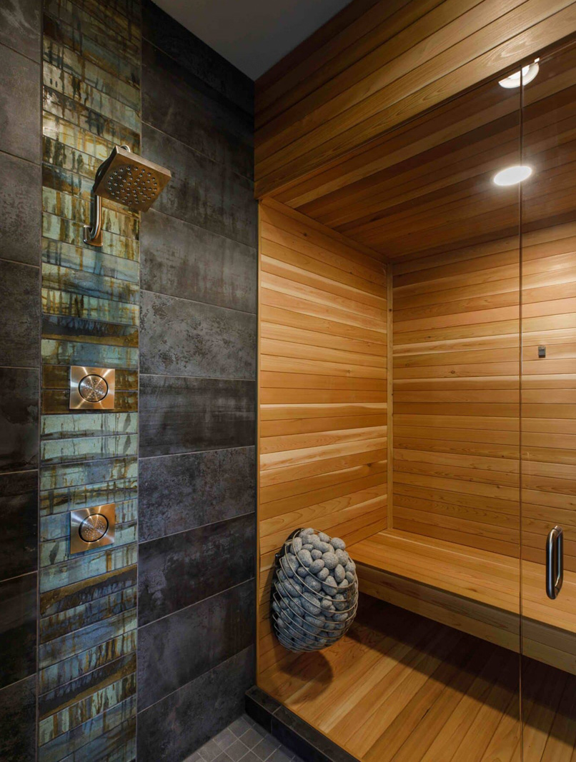 Modern sauna with wooden walls and a tiled shower area, featuring a rain showerhead and a cozy stone.