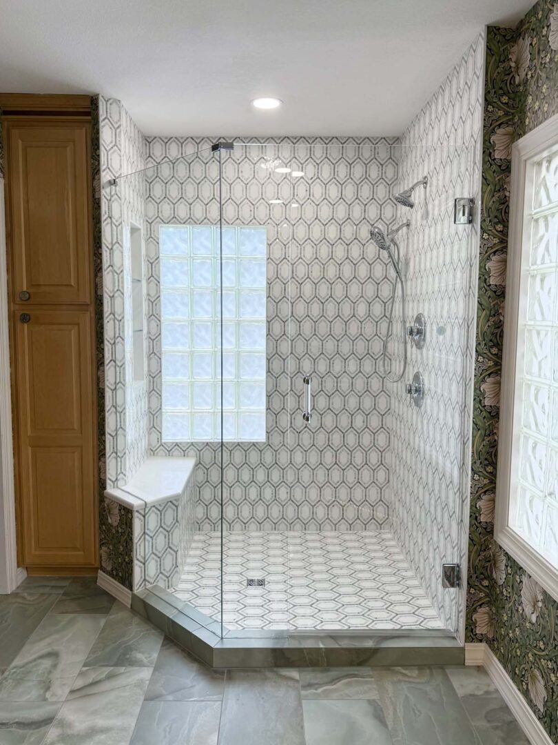 Spacious walk-in shower featuring clear glass walls, hexagonal patterned tiles, and a built-in bench.