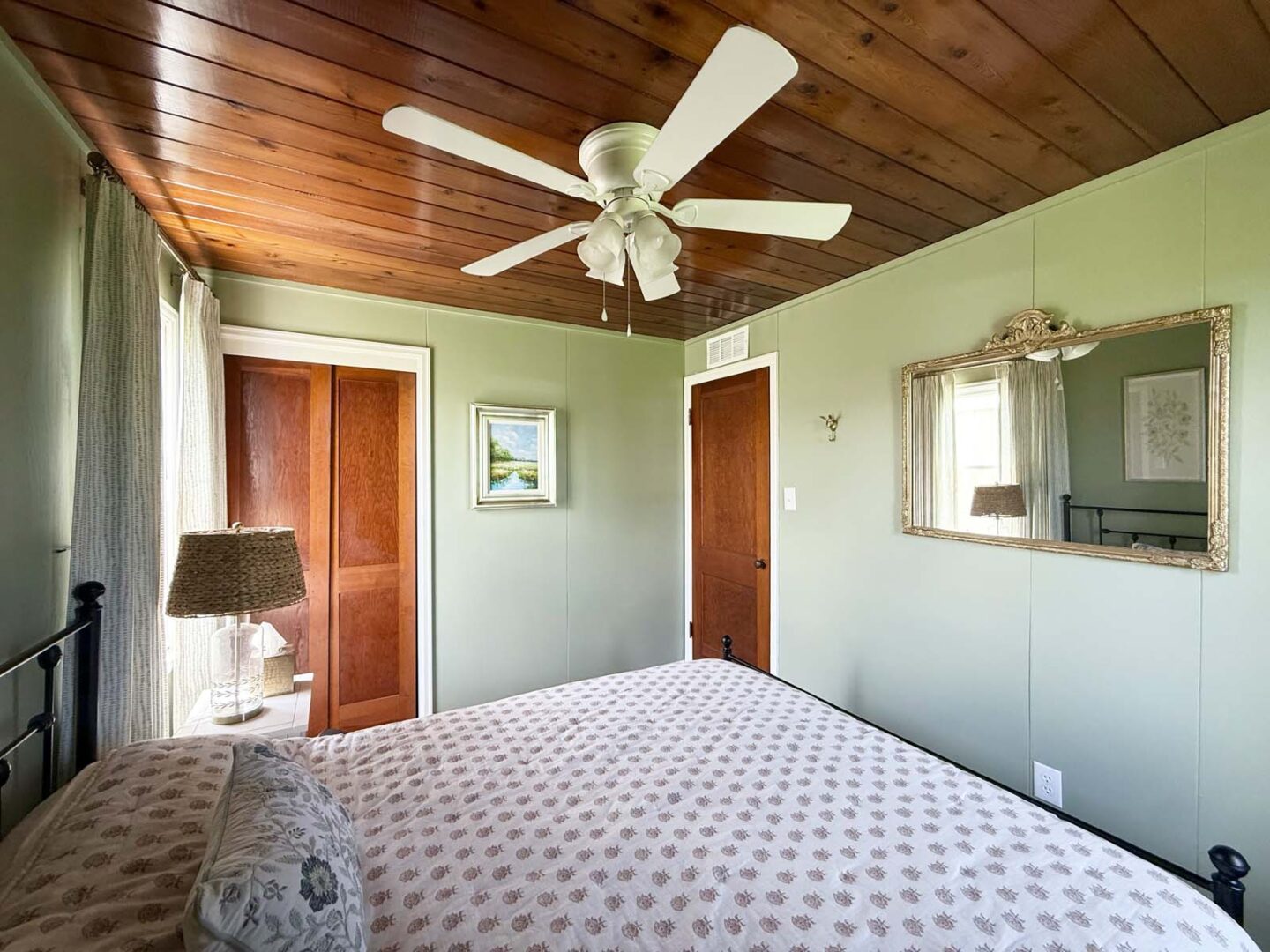 Interior bedroom design with green walls, wooden ceiling, and ceiling fan.