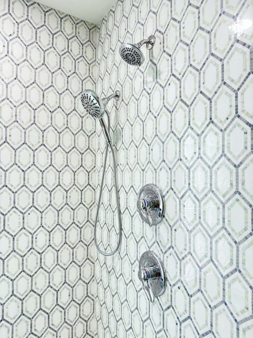 Bathroom shower with two showerheads and geometric tile design.