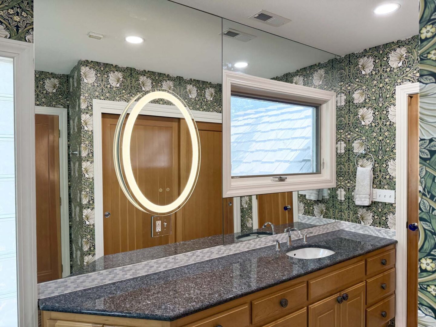 Modern bathroom with floral wallpaper, wooden cabinets, and a large mirror.