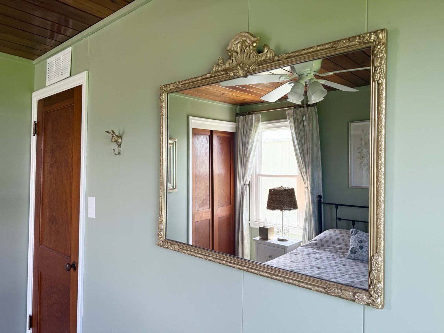 Vintage mirror reflecting a cozy bedroom with a bed, window, and ceiling fan.