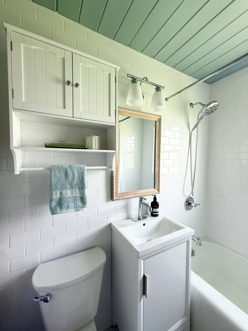 Bright bathroom featuring white subway tiles, a small vanity, and a shower with a handheld sprayer.