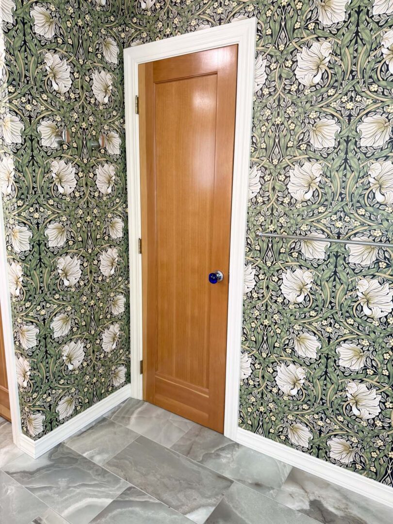 Classic wooden interior door with a blue doorknob set against floral wallpaper.