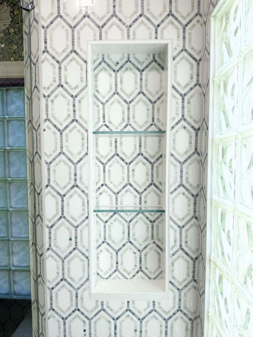 Geometric tile wall niche with glass shelves in a stylish interior space.