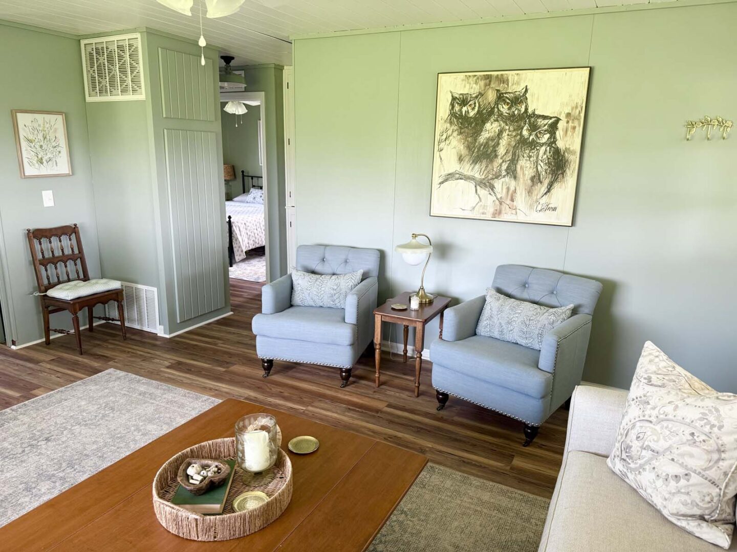 Cozy living room featuring light green walls, two blue armchairs, a wooden side table, and a large a.